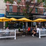 Diners sit outside on Arthur Ave, a white picket fence around the seating area
